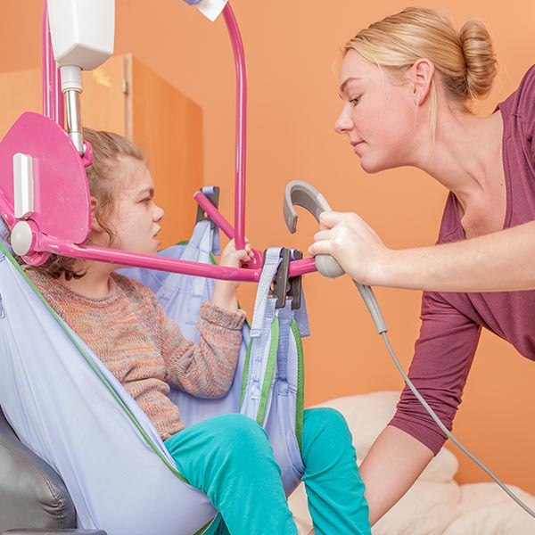 Nurse helping girl into bed with the assistance of special equipment