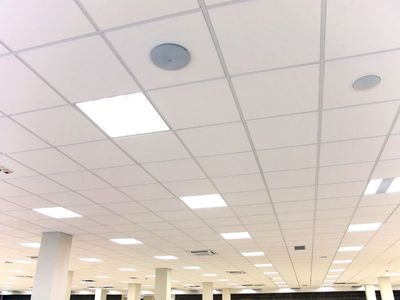 Modern drop ceiling grid in a commercial space featuring square recessed LED panel lights and circular speakers. Modern drop ceiling grid in a commercial space featuring square recessed LED panel lights and circular speakers.
